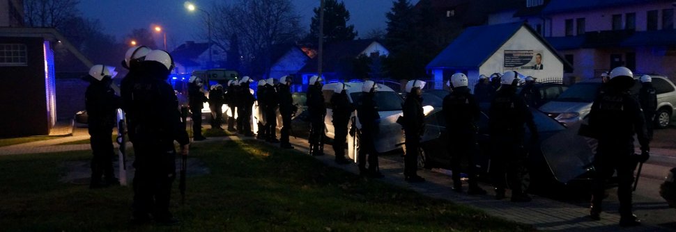 Na zdjęciu widoczni policjanci zabezpieczający imprezę masową, którzy stoją wzdłuż zaparkowanych samochodów. 