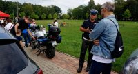 Na zdjęciu widoczny policjant wydziału ruchu drogowego, który rozmawia z mężczyzną, dalej osoby uczestniczące w &quot;Dniu bezpieczeństwa&quot; oglądają policyjny motocykl.