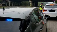 Umundurowany policjant wydziału ruchu drogowego grupy SPEED stoi przy zatrzymanym przy drodze białym samochodzie i rozmawia z kierujących, widać sygnał świetlny nieoznakowanego radiowozu.
