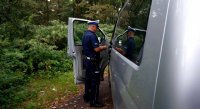 Na zdjęciu widoczny policjant wydziału ruchu drogowego z grupy SPPED , który rozmawia kierującym i przegląda jego dokumenty, obok widoczne krzaki i drzewa.
