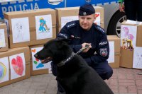 Na zdjęciu widoczny przewodnik oraz jego pies służbowy, w tle widoczne kartony z darami dla zwierząt.
