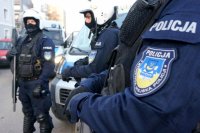 Na pierwszym planie widoczna naszywka Komendy Miejskiej Policji w Tycach, dalej widocznych dwóch policjantów w kaskach jeden z nich trzyma broń gładkolufową.