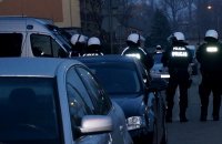 Na zdjęciu widoczne zaparkowane samochody oraz stojących tyłem do zdjęcia policjantów zabezpieczających imprezę masową w kaskach.