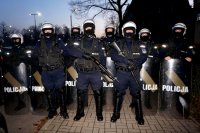 Na zdjęciu ośmiu policjantów zabezpieczających imprezę masową w kaskach i tarczach, dwóch stojących z przodu trzyma groń gładkolufową.