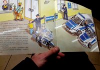 Otwarta strona z książki, na której są obrazki policjanta i radiowozów.