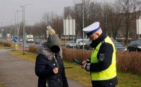 Policjant wydziału ruchu drogowego przekazuje kobiecie opaskę odblaskową.