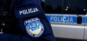 Na zdjęciu umundurowany policjant stojący przy radiowozie. Na rękawie munduru naszywka z napisem o treści: Policja Komenda Miejska Policji w Tychach oraz herb miasta Tychy.
