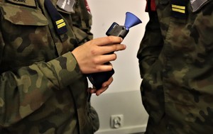 Na zdjęciu uczniowie w szkolnych mundurach. Jeden z uczniów trzyma urządzenie do badania stanu trzeźwości.