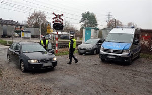 Na zdjęciu umundurowani policjanci stojący przy samochodzie osobowym. W tle tory kolejowe oraz radiowóz.