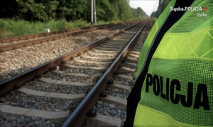 Na zdjęciu tory kolejowe oraz fragment umundurowania policyjnego- kamizelka odblaskowa z napisem Policja.