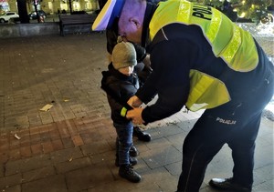 Na zdjęciu umundurowany policjant wręczający odblaski dziecku.