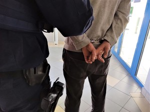 Na zdjęciu umundurowani policjanci z zatrzymanym mężczyzną